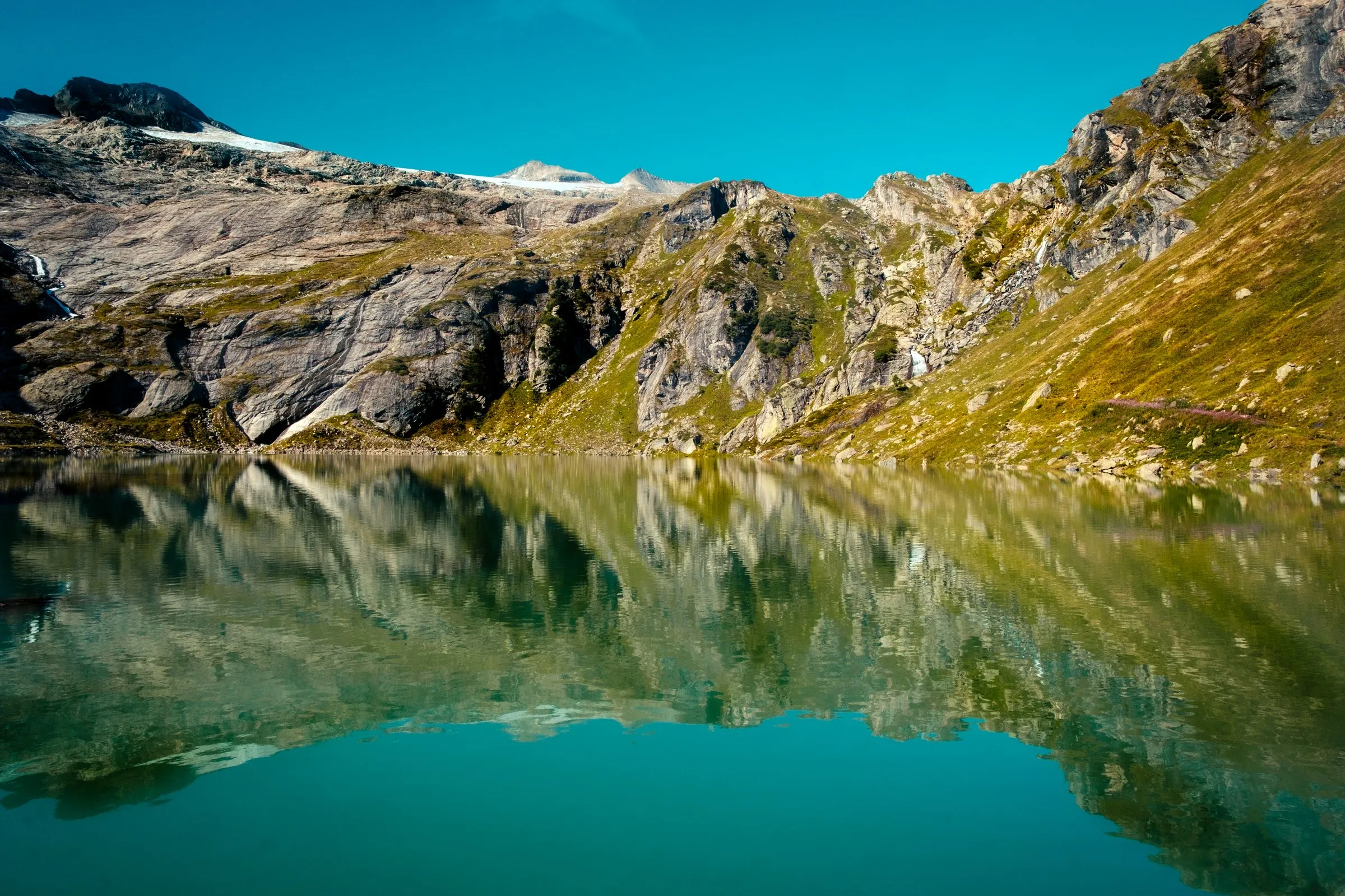 Bergsee, in dem sich Felsen und Almwiesen spiegeln