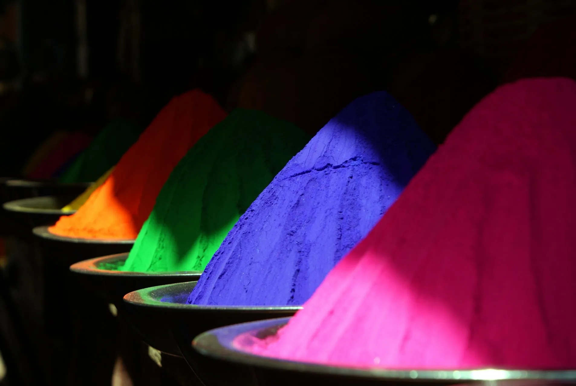 Schalen mit kegelförmig aufgehäuften Farbpigmenten in Orange, Grün, Blau und Pink