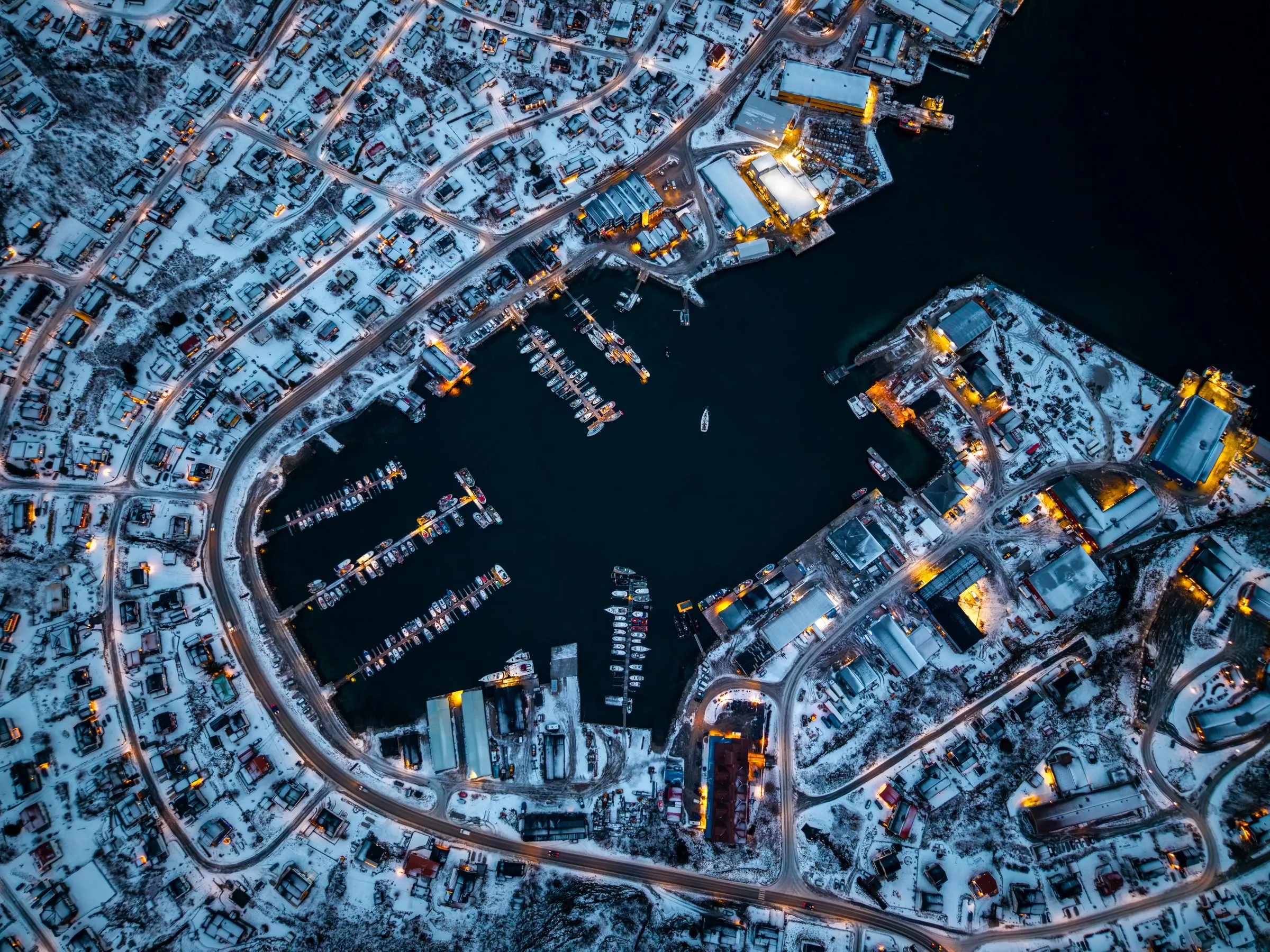Luftbild eines verschneiten Hafenorts bei Nacht mit beleuchteten Straßen