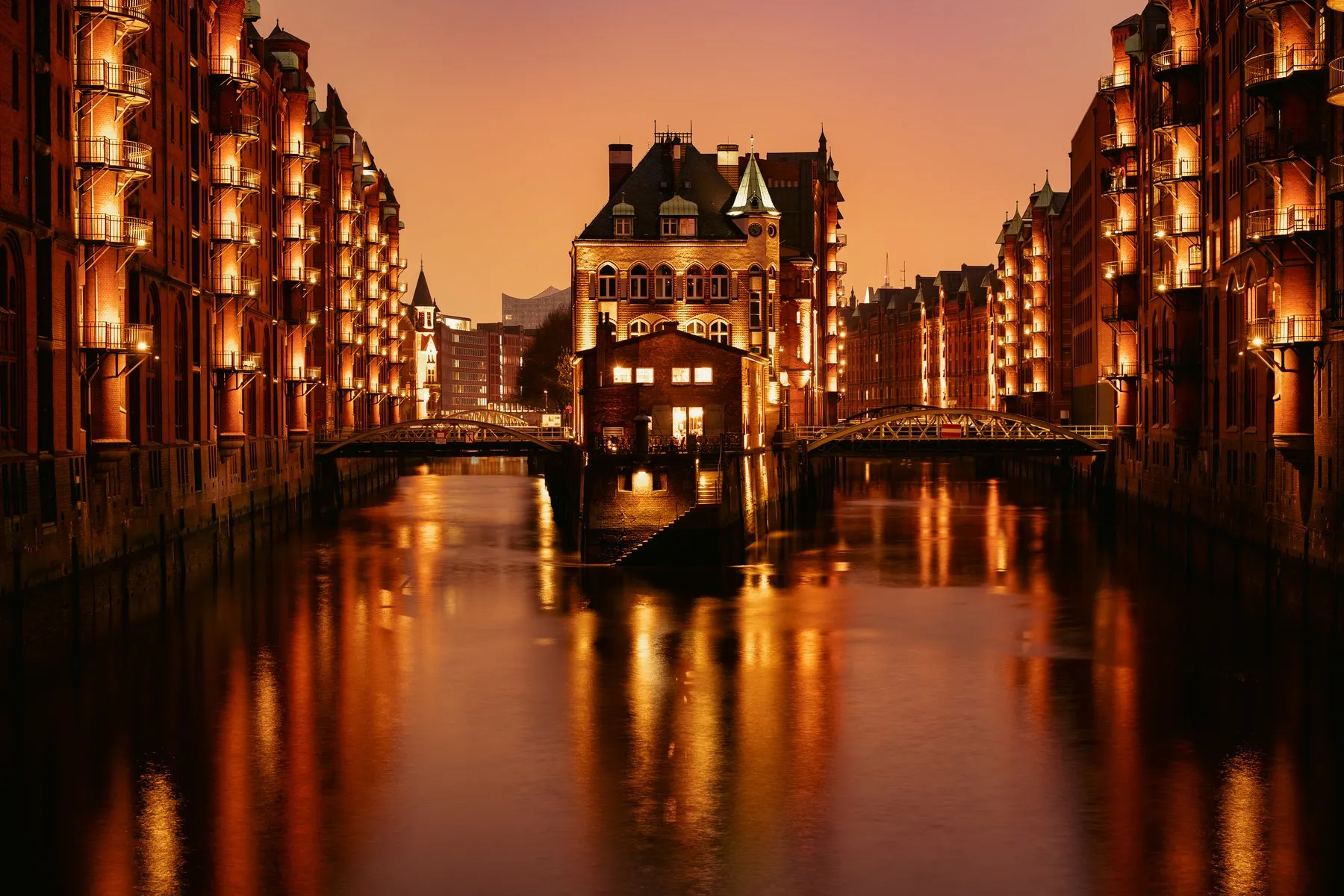 Hamburger Speicherstadt bei Nacht: beleuchtete Backsteinspeicher und das Wasserschloss spiegeln sich im Fleet